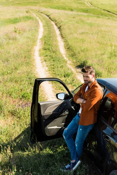 Vista elevada del joven con las manos cruzadas de pie cerca de su coche en el campo - foto de stock