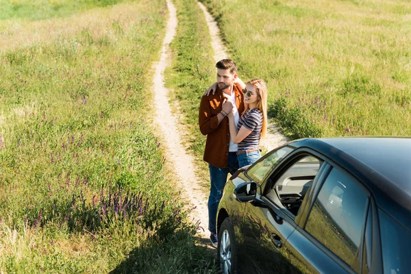 Vista elevada de pareja joven y elegante abrazando cerca de coche en el campo rural - foto de stock