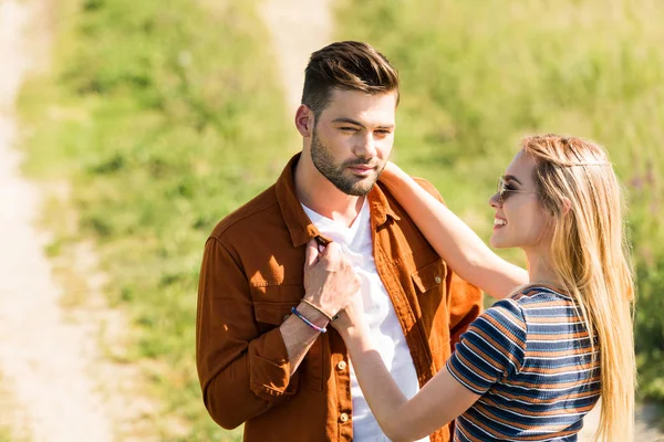 Young smiling woman in sunglasses embracing boyfriend in field — Stock Photo