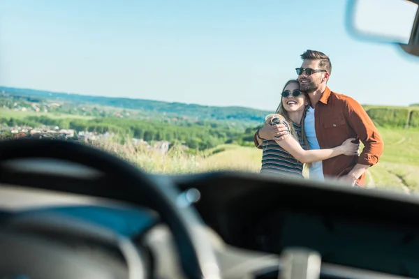 Vista frontal de la elegante pareja en gafas de sol abrazándose en el prado rural - foto de stock
