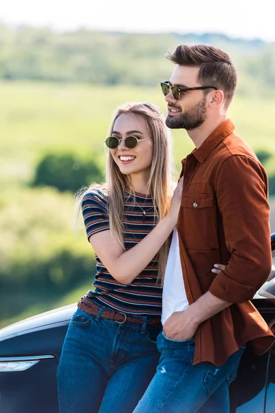 Happy stylish couple in sunglasses standing near car — Stock Photo