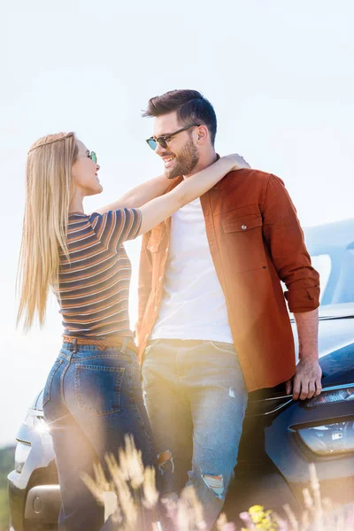 Seitenansicht einer jungen Frau, die ihren Freund mit Sonnenbrille in der Nähe des Autos umarmt — Stockfoto