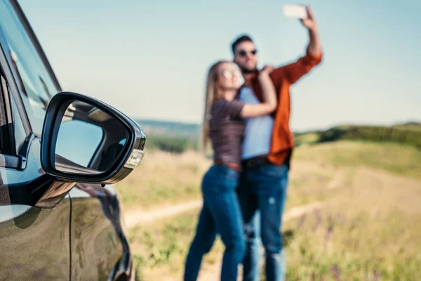Закрыть вид бокового зеркала автомобиля и пары, делающие селфи на размытом фоне — стоковое фото