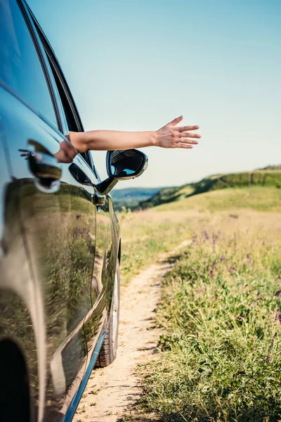 Cropped shot of woman leaning out hand from car window in rural field — Stock Photo