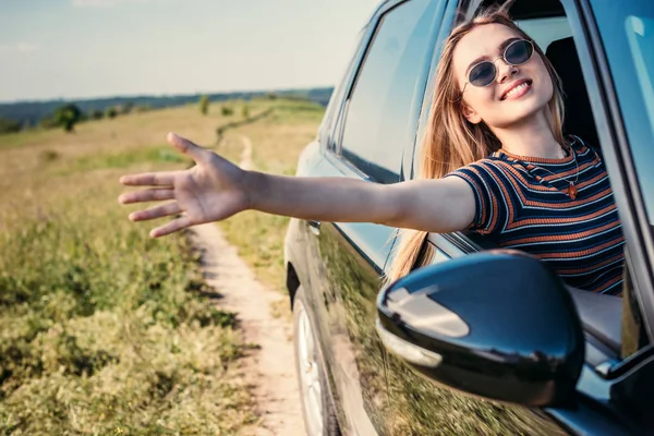 Стильна жінка в сонцезахисних окулярах, що випрямляє руку з вікна автомобіля — стокове фото