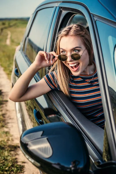 Vista frontal de la joven excitada inclinándose por la ventana del coche - foto de stock