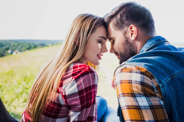 Vue de côté du jeune couple assis front au front sur le coffre de la voiture dans le domaine rural — Photo de stock