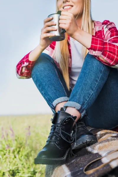 Imagen recortada de mujer joven sentada en el maletero del coche con taza de café en el campo rural - foto de stock