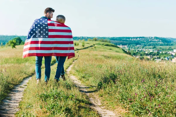 Rear view of young couple with american flag on rural meadow, independence day concept — Stock Photo