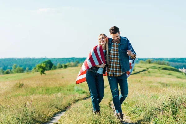 Feliz jovem casal com bandeira americana no prado rural, conceito de dia de independência — Fotografia de Stock