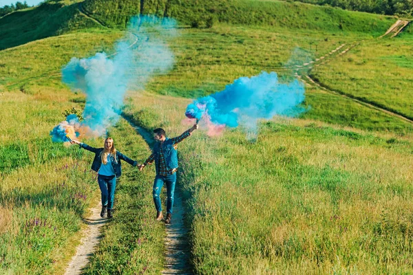 Vista elevada do casal segurando bombas de fumaça coloridas no prado rural — Fotografia de Stock