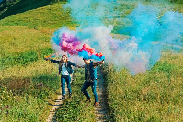 Visão de alto ângulo do casal segurando bombas de fumaça coloridas no prado rural — Fotografia de Stock