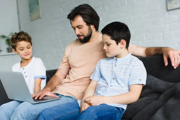 Father and sons near by using laptop together on sofa at home — Stock Photo