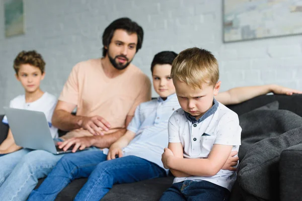 Selective focus of upset little boy and family man with laptop near by on sofa at home — Stock Photo
