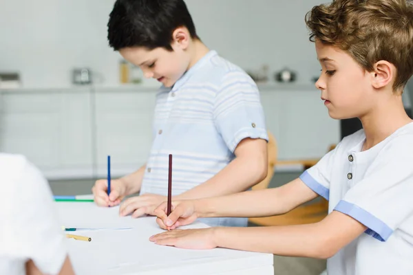 Vue latérale de petits frères dessinant des images à table à la maison — Photo de stock