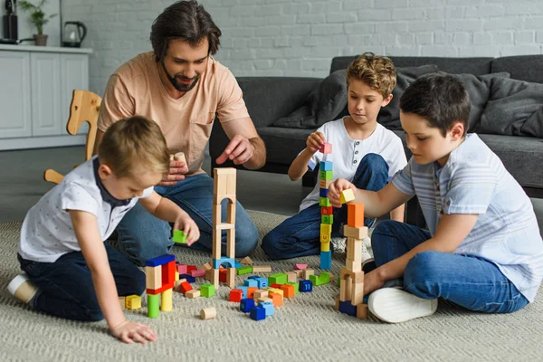 Father and kids playing with wooden blocks together on floor at home — Stock Photo