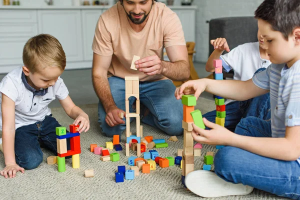 Vista parcial de padre e hijos jugando con bloques de madera juntos en el suelo en casa - foto de stock