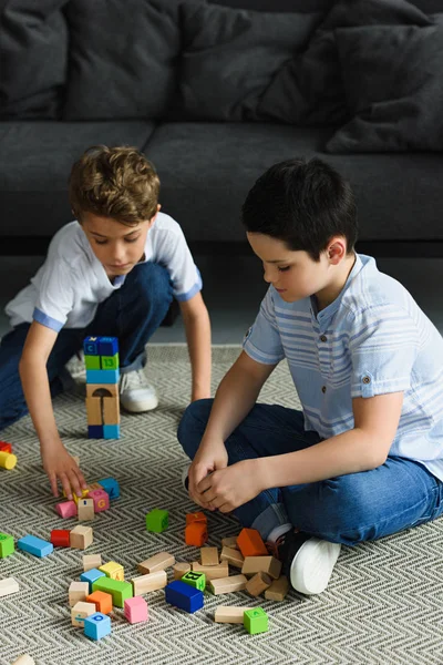 Niños pequeños jugando con bloques de madera en el suelo en casa - foto de stock
