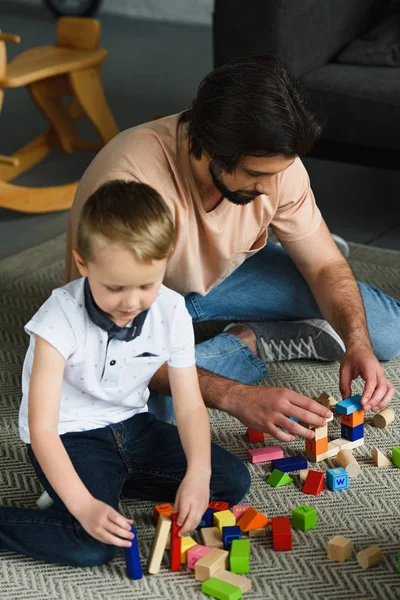 Pai e filho focados brincando com blocos de madeira juntos em casa — Fotografia de Stock