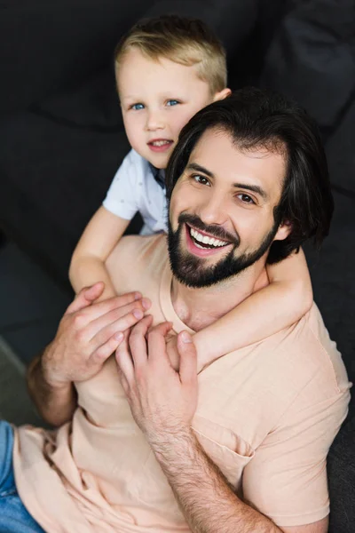 Blick aus der Vogelperspektive: Kleiner Sohn umarmt glücklichen Vater auf dem heimischen Sofa — Stockfoto