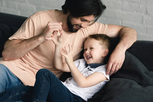 Glücklicher Vater und kleiner Sohn haben gemeinsam Spaß auf dem heimischen Sofa — Stockfoto