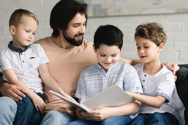 Retrato del padre y los hijos leyendo el libro juntos en casa - foto de stock