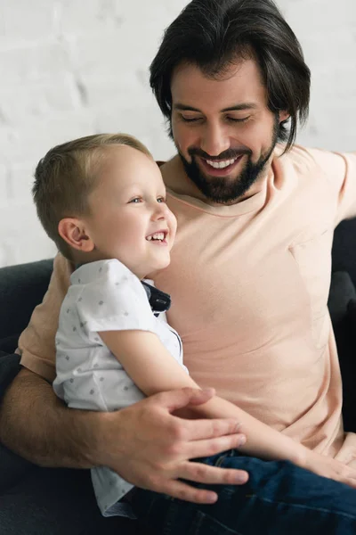 Porträt eines glücklichen Vaters, der seinen kleinen Sohn zu Hause auf dem Sofa umarmt — Stockfoto