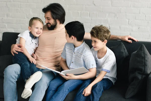 Портрет улыбающегося отца и сыновей, читающих книгу вместе дома — стоковое фото