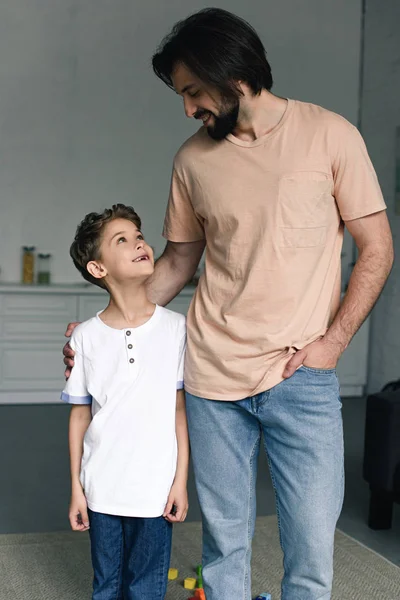 Портрет улыбающегося мальчика и отца, смотрящих друг на друга дома — стоковое фото