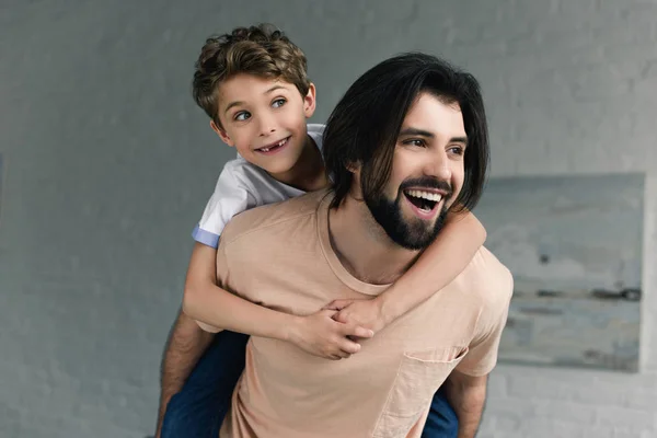 Portrait of happy father and little son piggybacking together at home — Stock Photo