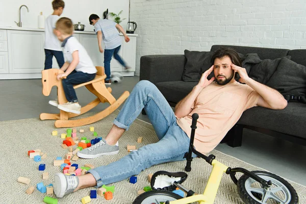Stressed father sitting on floor and kids playing around in room — Stock Photo