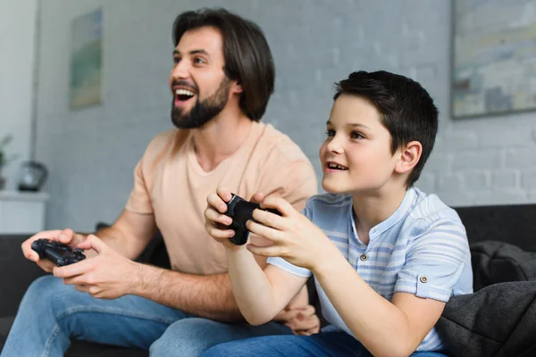 Side view of smiling father and son playing video games together at home — Stock Photo