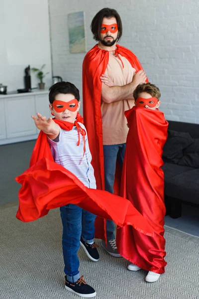 Man and cute little sons in red superhero costumes at home — Stock Photo
