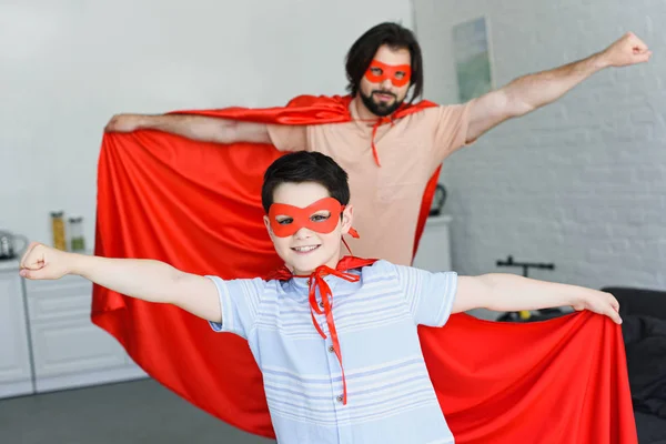 Enfoque selectivo de pequeño hijo y padre en trajes de superhéroe rojo en casa - foto de stock
