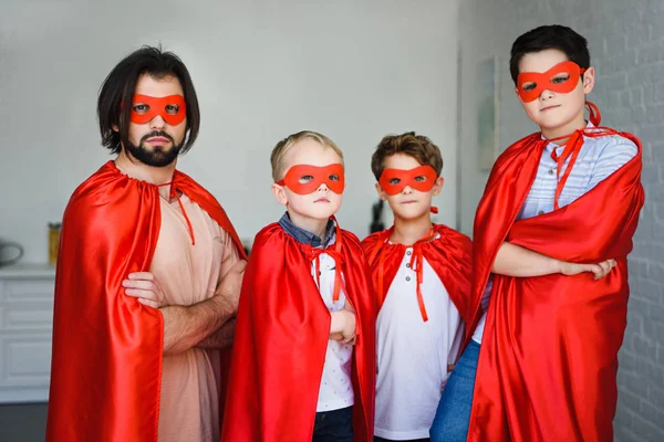 Portrait of father and little sons in red superhero costumes with arms crossed at home — Stock Photo