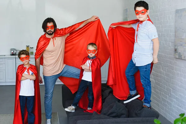 Sorrindo pai e filhos pequenos em trajes de super-herói vermelho em casa — Fotografia de Stock