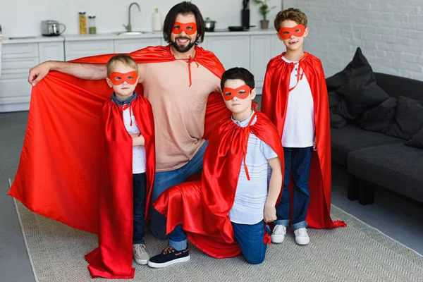 Smiling father and little sons in red superhero costumes at home — Stock Photo