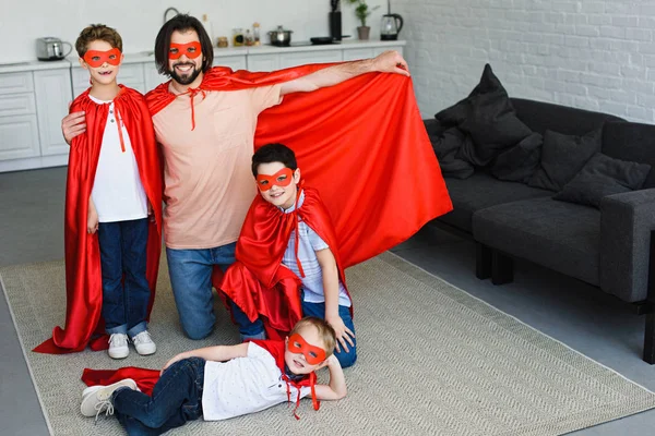 Sorrindo pai e filhos em trajes de super-herói vermelho em casa — Fotografia de Stock