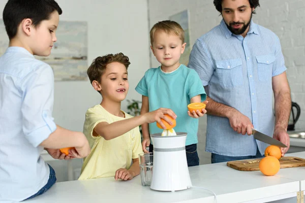 Familia haciendo zumo de naranja fresco juntos en la cocina en casa - foto de stock