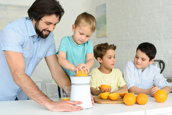 Familia haciendo zumo de naranja fresco juntos en la cocina en casa - foto de stock