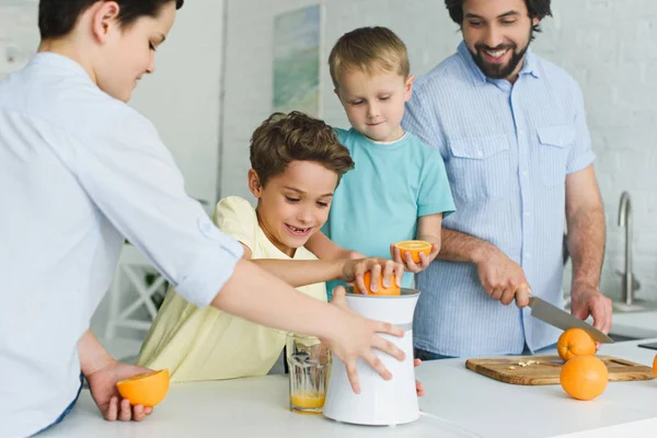 Famiglia felice facendo succo d'arancia fresco in cucina a casa — Foto stock