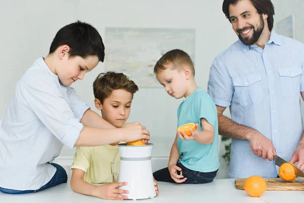 Retrato de padre e hijos haciendo zumo de naranja fresco en la cocina en casa - foto de stock