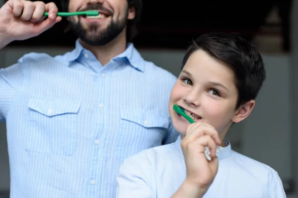 Vista parcial de padre e hijo cepillándose los dientes juntos en casa - foto de stock