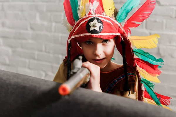 Kleiner Junge im Indianerkostüm mit Spielzeugpistole spielt zu Hause — Stockfoto