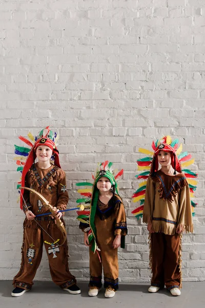 Niedliche kleine Jungen in indigenen Kostümen stehen vor weißen Ziegelwänden — Stockfoto