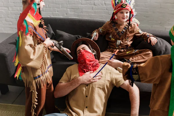 Mann mit Hut und rotem Kopftuch spielt zu Hause mit Söhnen in indigenen Kostümen — Stockfoto
