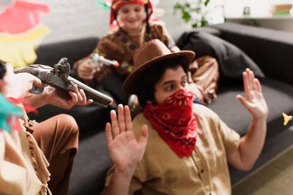 Man in hat and red bandana playing together with sons in indigenous costumes at home — Stock Photo