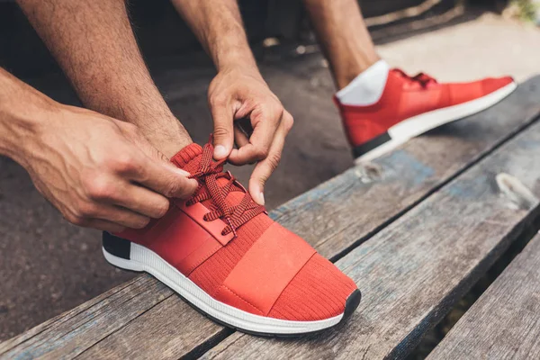 Cropped shot of sportsman tying shoelaces while sitting on bench at sport playground — Stock Photo