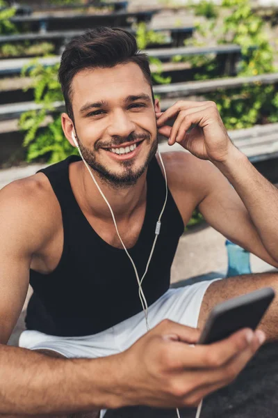 Retrato de joven deportista feliz escuchando música con smartphone y auriculares - foto de stock