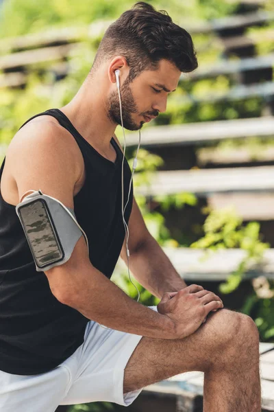 Joven deportista en auriculares con teléfono inteligente en caso de correr brazalete haciendo ejercicio - foto de stock